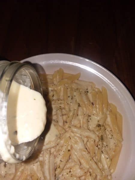 pouring Alfredo sauce on pasta noodles
