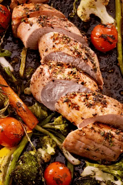 pork tenderloin on a cutting board with tomatoes, broccoli, and carrots.