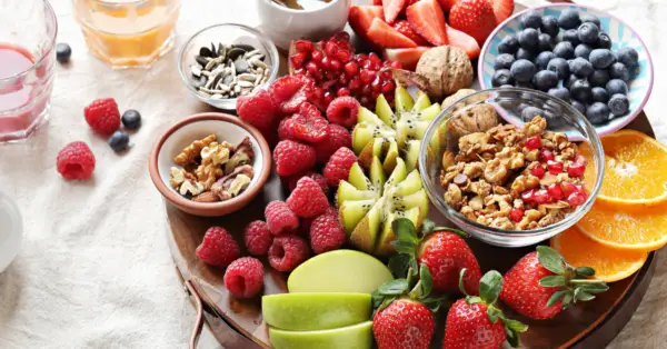 breakfast board with raspberries, blueberries, nuts, apples, and kiwis.