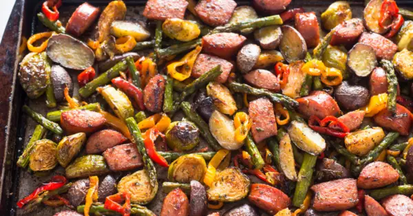 brussels sprouts, sweet potatoes, potatoes, sausages on a baking pan